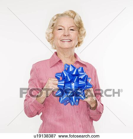 Stock Photo - Caucasian senior woman holding blue bow smiling at viewer.. Fotosearch