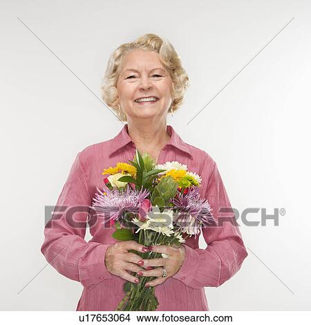Picture - Caucasian senior woman holding bouquet of flowers and smiling at viewer.. Fotosearch