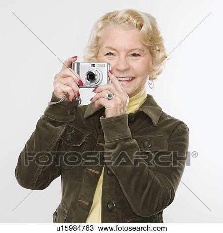 Stock Image - Caucasian senior woman taking photo with digital camera of viewer.. Fotosearch
