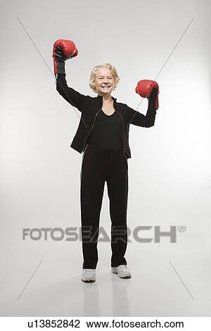 Stock Image - Caucasian senior woman wearing boxing gloves raised in the air.. Fotosearch