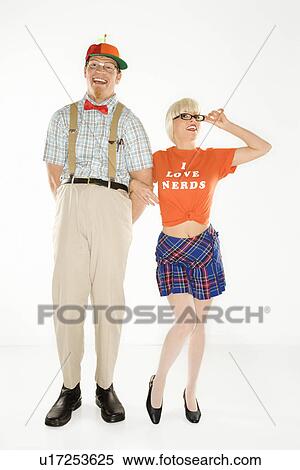 Stock Photography - Caucasian young man dressed like nerd wearing propeller hat with blonde Caucasian young woman in nerdy eyeglasses and tshirt reading I love nerds and plaid skirt.. Fotosearch