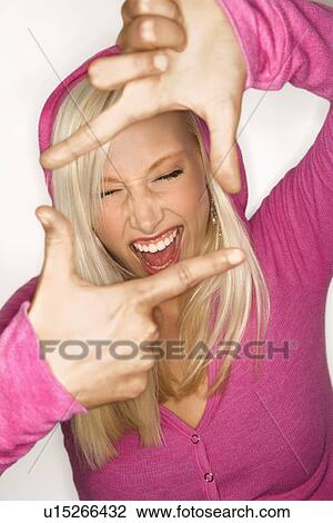 Stock Image - Portrait of attractive blonde Caucasian young adult woman wearing fuchsia holding hands up to make frame around face.. Fotosearch