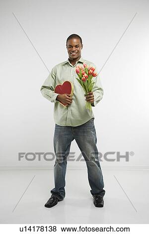 Studio shot of African-American man holding valentine heart and bouquet of tulips smiling and looking at viewer. View Large Photo Image Stock Photo - Studio shot of African-American man holding valentine heart and bouquet of tulips smiling and looking at viewer.. Fotosearch