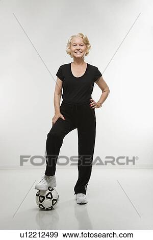 Stock Photo - Woman standing with foot on soccer ball. Fotosearch