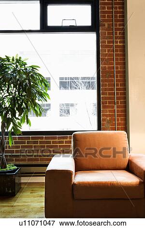 Cushy chair in loft apartment with houseplant in front of window. View Large Photo Image Stock Photo - Cushy chair in loft apartment with houseplant in front of window.. Fotosearch