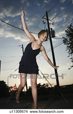Picture - Caucasian mid-adult blonde woman wearing little black dress posing in street at sunset.. Fotosearch