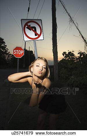 Stock Photo - Caucasian mid-adult blonde woman wearing little black dress blowing kiss at viewer beside no left turn sign and stop sign.. Fotosearch