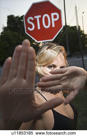 Stock Photography - Caucasian mid-adult blonde woman holding hands up to camera in front of stop sign.. Fotosearch
