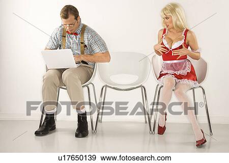 Stock Photo - Caucasian young man dressed like nerd sitting with laptop with Caucasian young blonde woman trying to distract him with cleavage.. Fotosearch