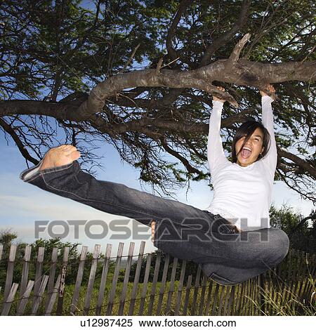 Stock Photography - Female holding on to tree and kicking air and screaming. Fotosearch