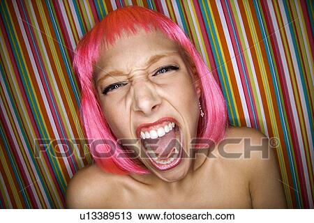 Stock Image - Portrait of attractive Caucasian young adult woman wearing pink wig against striped background making sassy expression at viewer.. Fotosearch