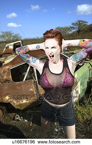 Sexy tattooed woman yelling and holding her hands over her ears in junkyard View Large Photo Image Stock Photograph - Sexy tattooed woman yelling and holding her hands over her ears in junkyard. Fotosearch