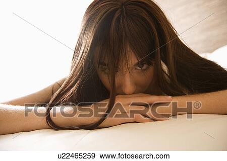Stock Photo - Pretty young Caucasian woman lying on bed making eye contact.. Fotosearch