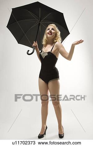 Stock Image - Attractive Caucasian woman wearing retro swimsuit in pinup pose with umbrella.. Fotosearch