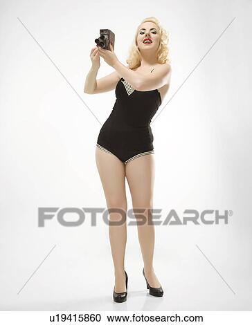 Stock Image - Attractive Caucasian woman wearing retro swimsuit in pinup pose with vintage camera.. Fotosearch