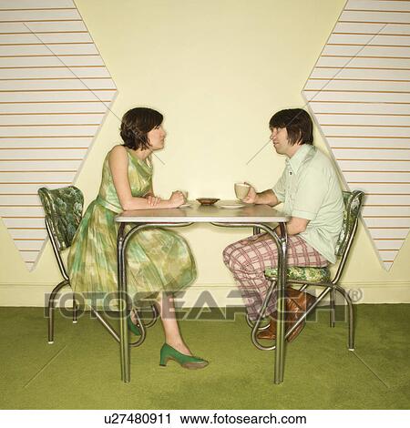 Stock Image - Caucasian mid-adult man and woman wearing vintage clothing sitting at 50's retro dinette set facing each other.. Fotosearch