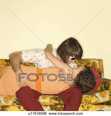 Stock Photograph - Couple smiling and embracing on colorful retro sofa.. Fotosearch