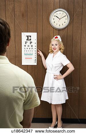 Stock Photo - Female nurse pointing out eye chart to mid-adult male patient. Fotosearch