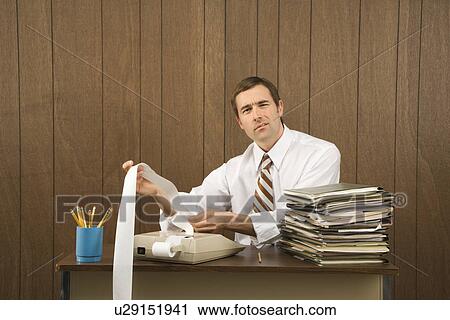 Stock Image - Mid-adult Caucasian male holding printout from calculator in office setting.. Fotosearch