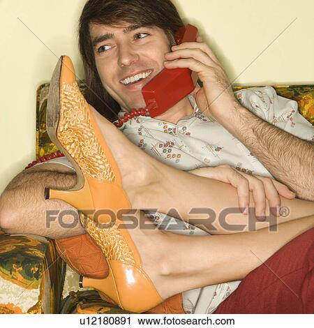 Stock Image - Mid-adult man talking on telephone with mid-adult woman's legs draped over lap. Fotosearch