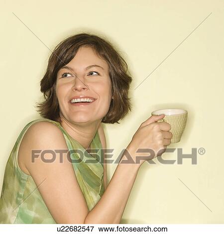 Stock Photo - Pretty mid-adult woman holding up coffee cup and smiling. Fotosearch