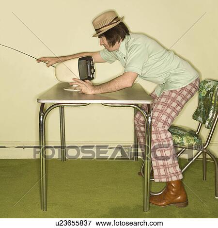 Side view of Caucasian mid-adult man wearing hat and plaid pants leaning over 50's retro dinette set adjusting old television set. View Large Photo Image Stock Photo - Side view of Caucasian mid-adult man wearing hat and plaid pants leaning over 50's retro dinette set adjusting old television set.. Fotosearch