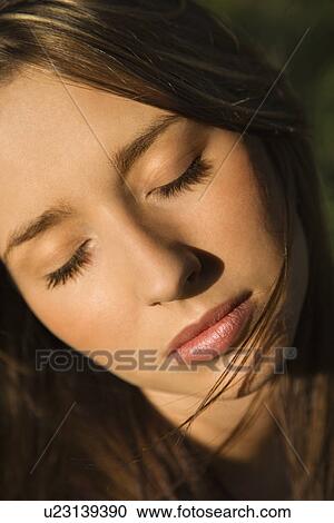 Stock Image - Close-up portrait of attractive young Caucasian woman with eyes closed and long brown hair.. Fotosearch