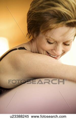 Stock Photography - Portrait of pretty woman draped over sofa by window looking down and smiling. Fotosearch