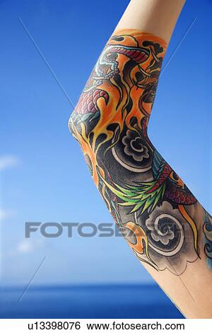 Stock Photograph - Close up of tattooed woman's arm with Pacific Ocean in background . Fotosearch