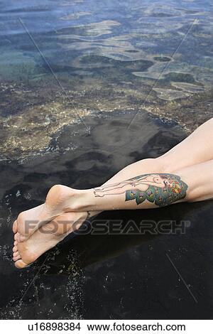 Picture - Legs of tattooed woman lying in tidal pool . Fotosearch