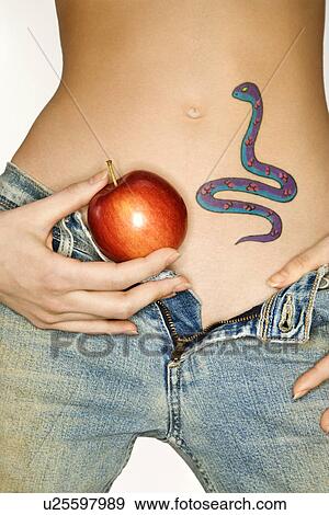 Portrait of attractive young woman holding apple by snake tattoo on stomach View Large Photo Image Stock Photo - Portrait of attractive young woman holding apple by snake tattoo on stomach. Fotosearch
