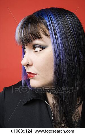 Picture - Portrait of woman with blue hair, tattoo, and spike collar looking to side against orange background. Fotosearch