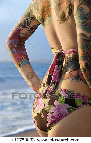 Stock Image - Side view of attractive Caucasian tattooed woman in bikini on beach . Fotosearch