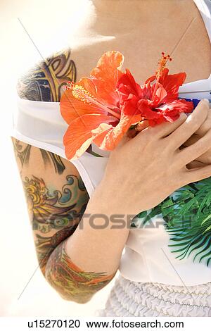 Stock Image - Tattooed woman holding Hibiscus flowers . Fotosearch