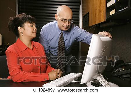 Stock Photo - Businessman and businesswoman in office looking at computer monitor.. Fotosearch