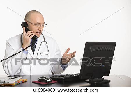 Stock Photo - Doctor looking at a computer while talking on a phone. Fotosearch