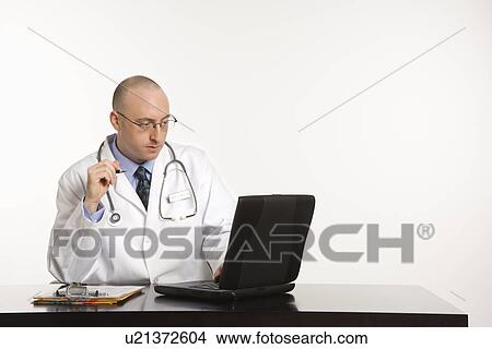 Doctor looking at a laptop computer View Large Photo Image Picture - Doctor looking at a laptop computer. Fotosearch