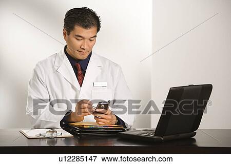 Man in a lab coat checking his phone View Large Photo Image Stock Photo - Man in a lab coat checking his phone. Fotosearch