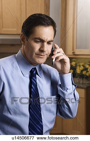 Stock Photo - Man in business apparel on a cellphone in the kitchen. Fotosearch