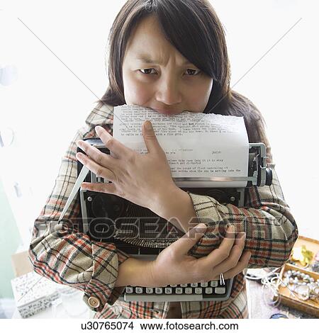 Picture - Pretty young woman holding typewriter and biting page. Fotosearch