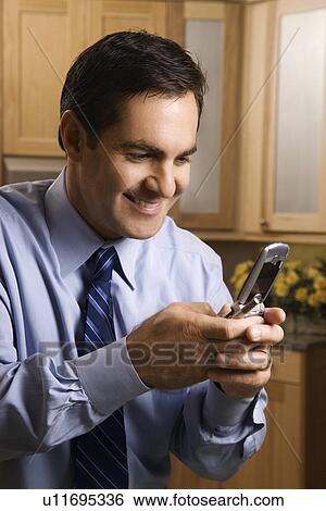Stock Photograph - Smiling businessman holding his cellphone in the kitchen. Fotosearch