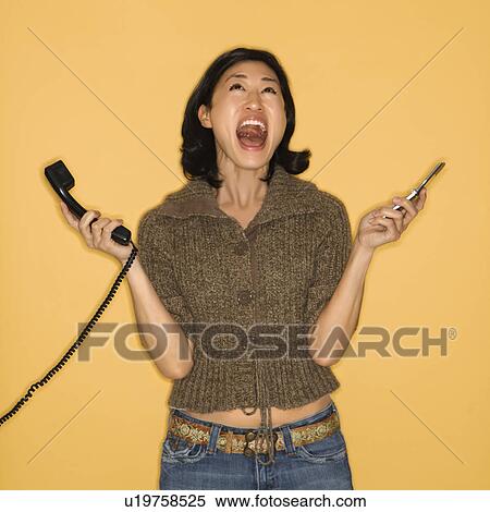 Stock Photography - Yelling woman holding two phones. Fotosearch
