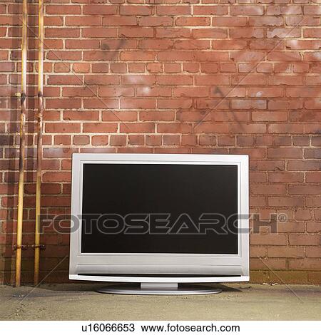 Stock Image - Flat panel television set in front of red brick wall. Fotosearch