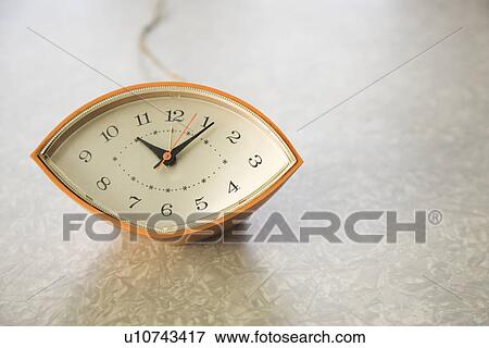 Stock Photo - Still life of orange eye-shaped vintage clock on table. Fotosearch