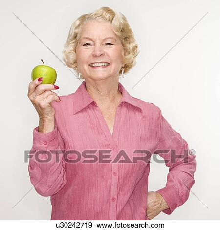 Stock Photo - Caucasian senior woman holding apple smiling at viewer.. Fotosearch