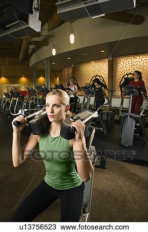 Stock Image - Female using exercise equipment at gym. Fotosearch