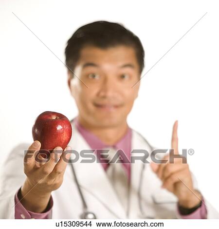 Picture - Male doctor holding out apple. Fotosearch