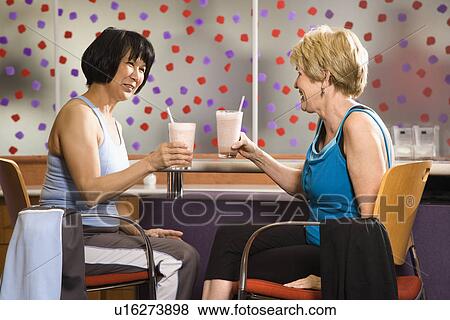 Mature Asian and Caucasian adult females sitting at table in health club cafeteria. View Large Photo Image Stock Photo - Mature Asian and Caucasian adult females sitting at table in health club cafeteria.. Fotosearch