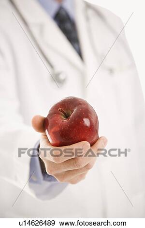Stock Photo - Mid adult male physician holding apple. Fotosearch