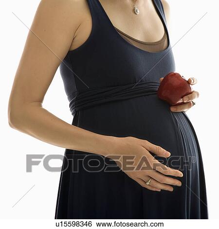 Stock Photograph - Portrait of Caucasion mid-adult pregnant woman with hands on belly holding an apple.. Fotosearch